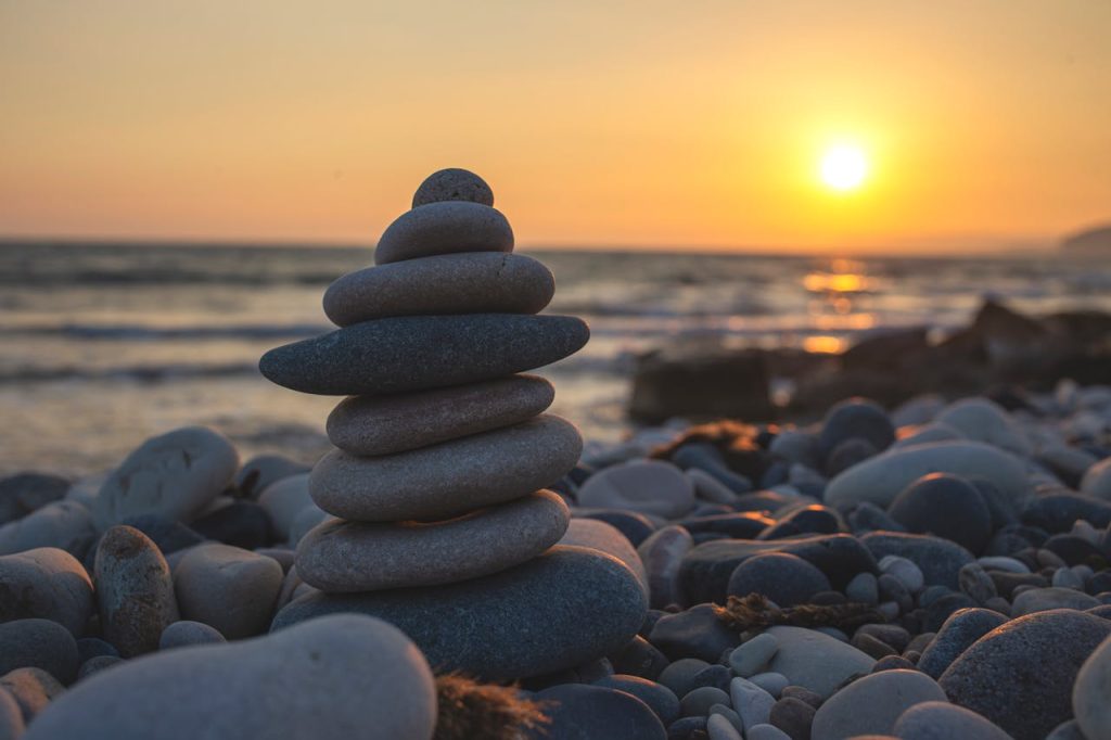 Tranquil sunset at the beach with stacked stone cairn and golden hour light, perfect for relaxation themes.
